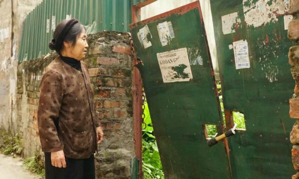Bà Lưu Thị Dong đứng trước khu vườn bị chặt phá và đang bị cô Bưởi đóng cửa lại
