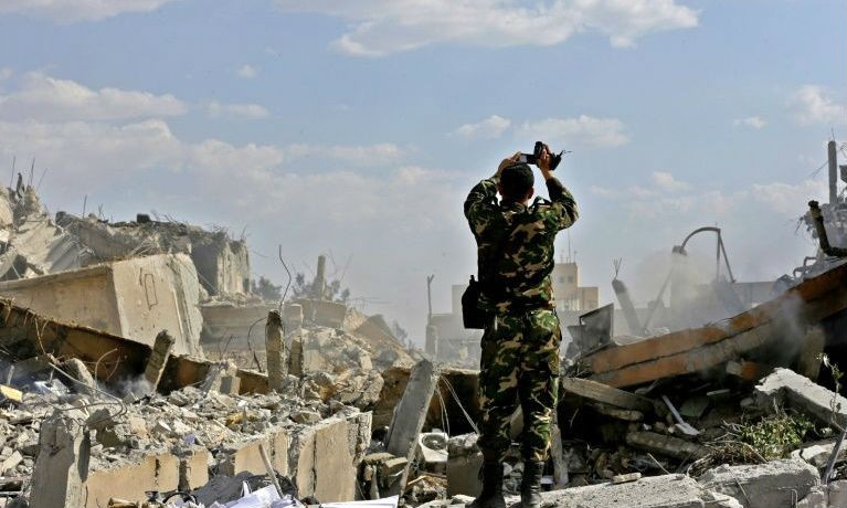 Một binh sỹ Syria kiểm tra một tòa nhà đổ nát sau cuộc không kích của Mỹ và các nước đồng minh