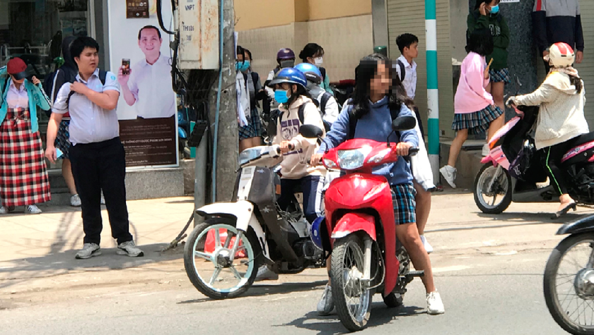 Một học sinh để đầu trần chạy xe máy rời cổng trường