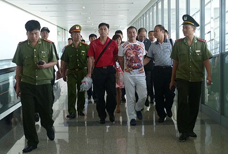 Lực lượng chức năng tiếp nhận, dẫn giải đối tượng truy nã Nguyễn Quốc Hùng (người mặc áo phông hoa ở giữa) tại sân bay quốc tế Nội Bài.