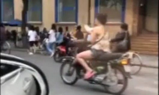 Cô gái vừa chạy xe máy vừa đọc sách trên đường phố Hà Nội