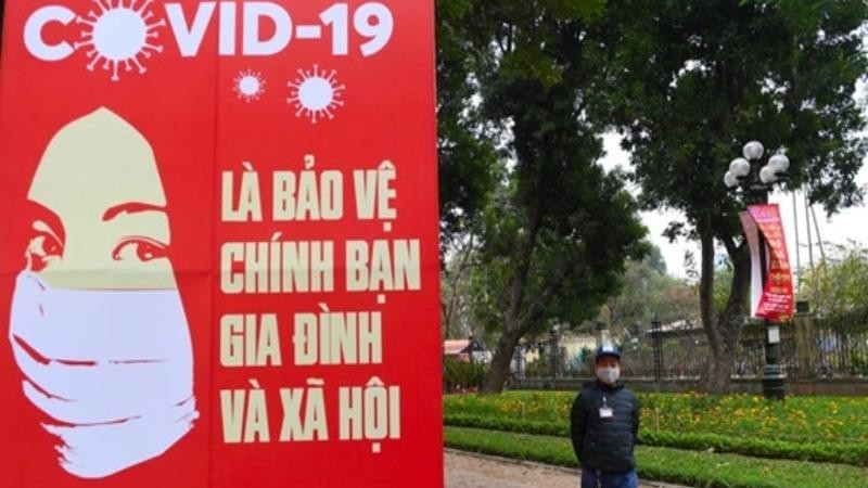 Người dân đeo khẩu trang đi qua biểu ngữ kêu gọi cộng đồng chung sức phòng, chống dịch Covid-19 tại Hà Nội. (Ảnh: Getty Images)