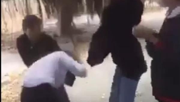 Một em mang áo khoác đen dùng mũ bảo hiểm đánh vào vùng đầu nữ sinh. 