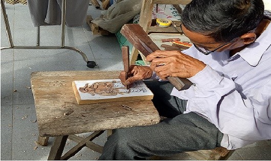 Nghệ nhân Kỳ Hữu Phước đang say sưa khắc bản gỗ, đảm bảo số lượng sản phẩm phục vụ Tết Nguyên đán cho bà con, du khách gần xa.