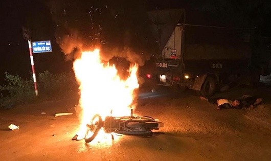 Chiếc xe máy của hai thanh niên bốc cháy dữ dội sau cú va chạm với xe tải.