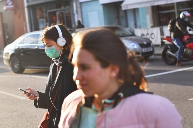 Người đi bộ băng qua đường khi một phụ nữ đeo mặt nạ bảo vệ ở London, Anh ngày 13/3. Ảnh: Reuters