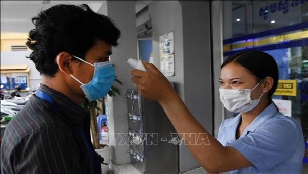 Nhân viên y tế kiểm tra thân nhiệt một khách hàng nhằm ngăn dịch COVID-19 lây lan, bên ngoài một ngân hàng ở Phnom Penh, Campuchia. Ảnh: AFP/TTXVN