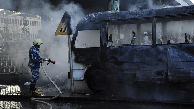 Một lính cứu hỏa Syria dập tắt một chiếc xe buýt bị cháy tại địa điểm xảy ra một vụ nổ chết người, ở Damascus, Syria, ngày 20/10/2021. Ảnh: Thông tấn xã Syria SANA phát qua AP