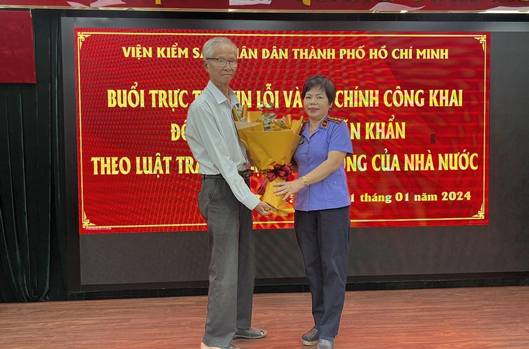 Bà Vũ Xuân Nhuệ, đại diện VKSND TP HCM (bên phải) tặng hoa cho ông Khẩn trong buổi xin lỗi. (Ảnh: Thiện Quang)