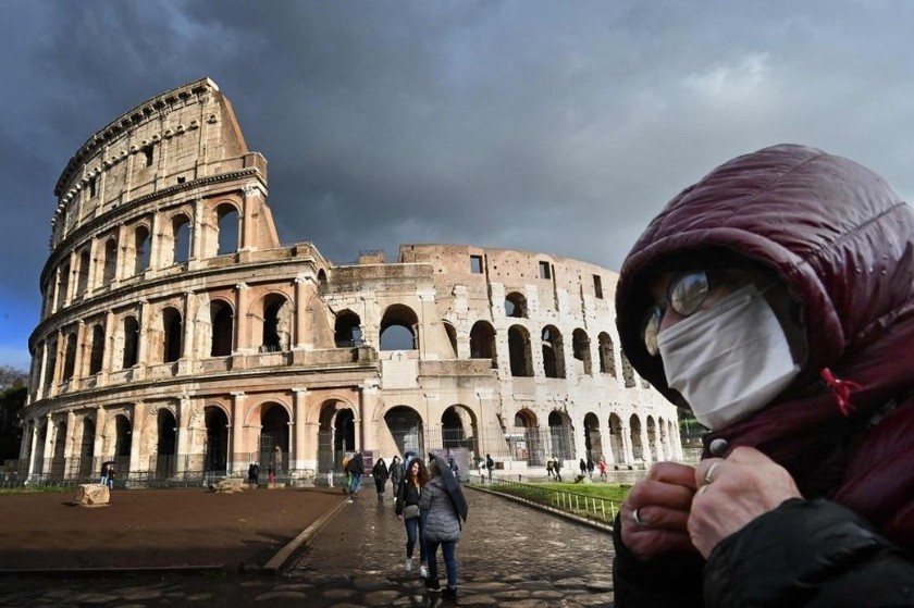 Du khách đeo khẩu trang đi qua trước đấu trường Coliseum ở Rome. Ảnh: AFP.