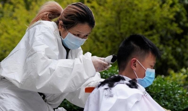 Thợ cắt tóc Quân Phương, 39 tuổi, cắt tóc của khách hàng tại một khu dân cư ở Vũ Hán, Hồ Bắc, Trung Quốc (COVID-19), ngày 30/3/2020. Ảnh: Reuters.
