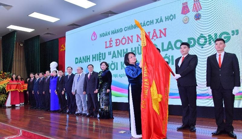 Phó Chủ tịch nước Đặng Thị Ngọc Thịnh đính huy hiệu “Anh hùng lao động” thời kỳ đổi mới lên lá cờ truyền thống của NHCSXH.