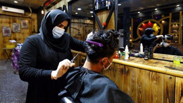 Thợ cắt tóc người Iraq đeo khẩu trang đang cắt tóc cho khách hàng. Ảnh: REUTERS.