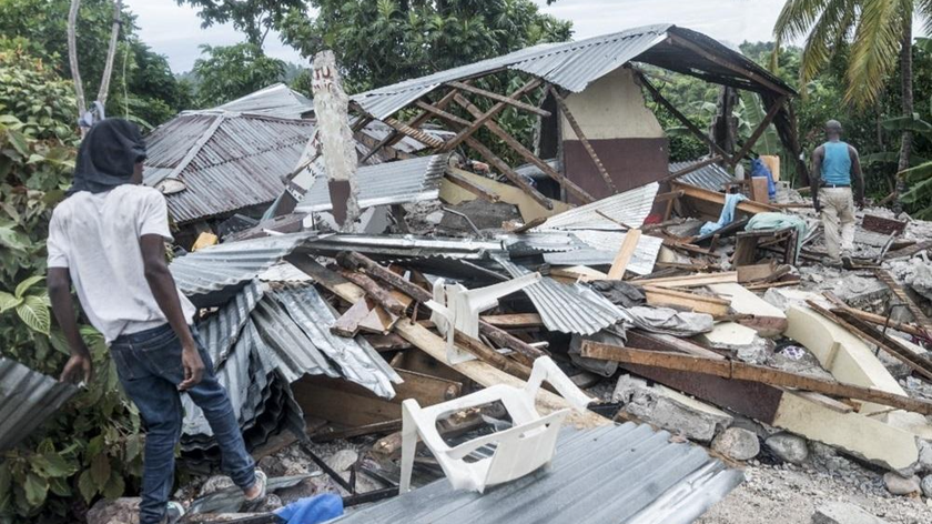 Người dân đứng cạnh một ngôi nhà bị phá hủy sau trận động đất gần Camp-Perrin, Haiti hôm 16/8. Ảnh: AFP.