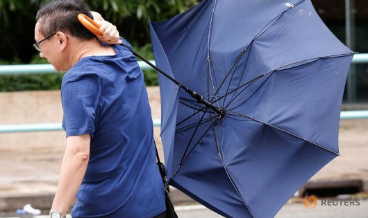  Một người đàn ông đang đi bộ trong cơn bão Nida bị gió hất tung ô. 