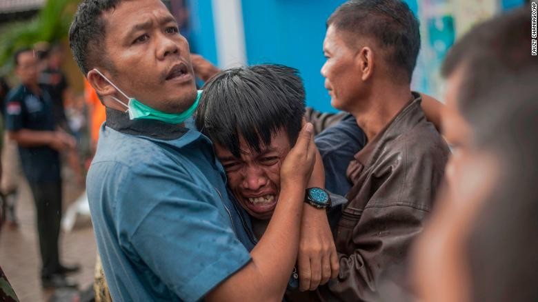 Người đàn ông gục ngã khi tìm thấy xác người thân do sóng thân trên bãi biển Carita, Indonesia.