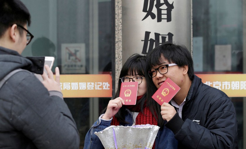 Một cặp đôi cầm giấy đăng ký kết hôn chụp ảnh bên ngoài văn phòng đăng ký ở Bắc Kinh, Trung Quốc. Ảnh: Reuters.